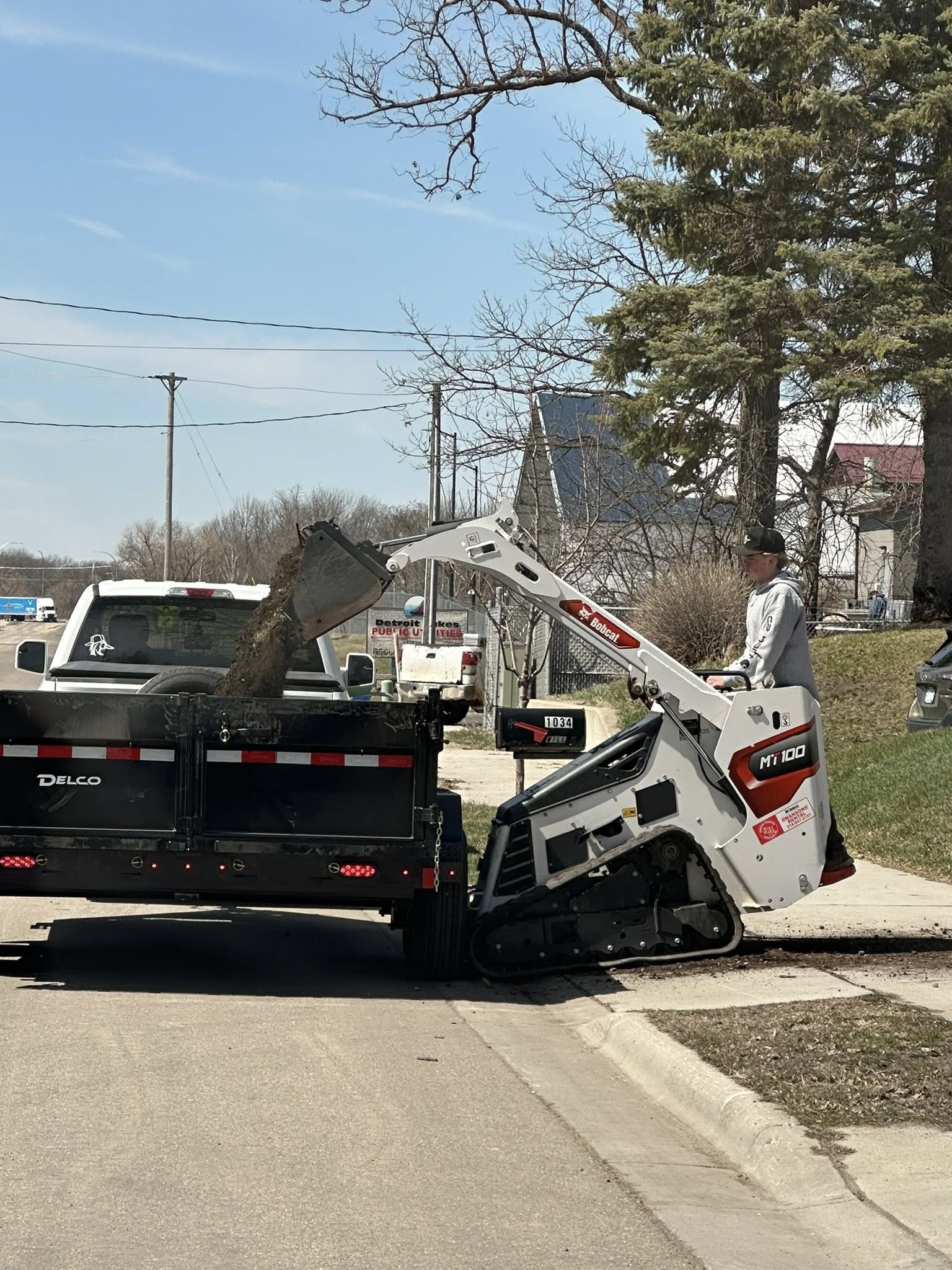 Compact track loader loading material into a trailer on a hardscaping job site